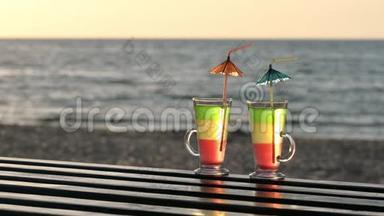 两杯鸡尾酒，在木制桌面上放吸管，进入海滩上的日落，背景是大海