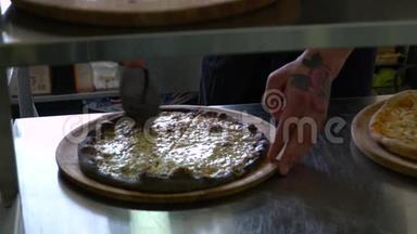 一个年轻的披萨师在餐厅的厨房准备披萨。 厨师用刀子把比萨饼切成碎片
