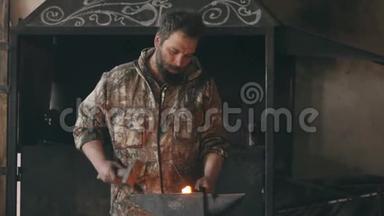 长胡子的青年铁匠在铁匠的铁砧上用火花烟火手工锻造铁水