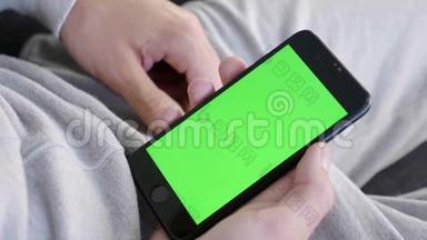 男人在家坐在沙发上，拿着绿色的模拟屏幕智能手机