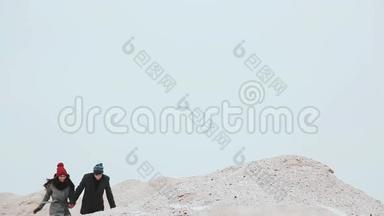 一个女孩和一个男人一起跑，手牵着手在沙丘上。