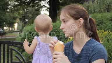 一个年轻女孩坐在长凳上，旁边站着一个穿着着一个穿着淡紫色连衣裙的小女孩，旁边有一个白色的圆点图案