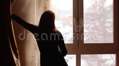 年轻女子在一间黑暗的房间里拉开窗帘，<strong>看窗外</strong>冬天的景色