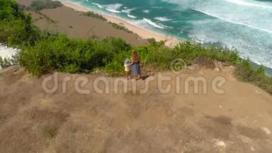 一名年轻女子和她的儿子在巴厘岛的一个偏僻的海滩上访问了纽约。 站在岩石上