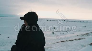 年轻女孩穿着黑色夹克，戴着帽子，坐在<strong>冰冻</strong>的海面上