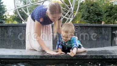 在公园的喷泉里，欢快的幼儿男孩在喷水池里和年轻的妈妈玩耍