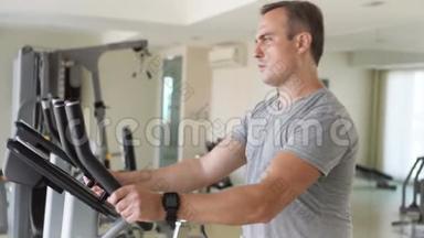 一个英俊健康的年轻人在健身房骑着健身车做运动。用他的智能手表检查生命体征