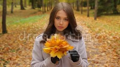 美丽的小姐在秋天的公园里等着一个人，用枫叶花束微笑着对一个人说