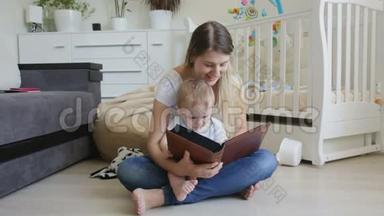 美丽的年轻母亲和她的小儿子坐在地板上，在相册里给他看家庭照片