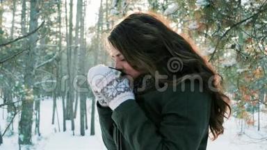年轻女子在冬林里喝茶，美丽的女孩在冬天在户外喝茶，可爱的女孩拿着杯子