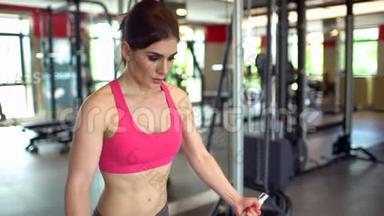 肌肉发达的女运动员穿着粉红色上衣在健身房锻炼举重。 健身女孩在健身房锻炼。 这就是