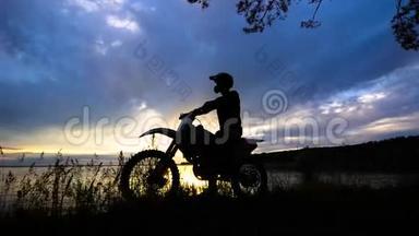 一位坐在摩托车上的极端交通司机的剪影，一辆车站在夕阳<strong>背景</strong>下的<strong>河边</strong>