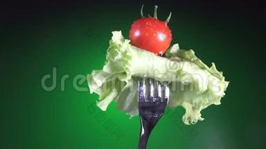 用新鲜的红番茄叉在水滴里，生菜旋转绿色背景