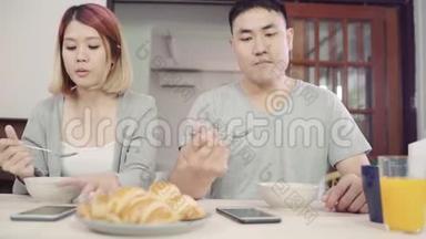 漂亮的亚洲年轻夫妇在吃<strong>早餐</strong>时，一边拿着报纸和手机，一边在<strong>桌子</strong>上分心。