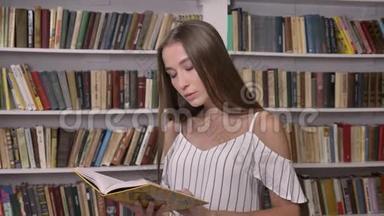 年轻迷人的女孩正在图书馆看书，看着镜头，微笑着