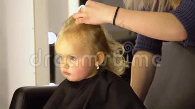 一个在美容院的小孩。 漂亮的女孩坐在椅子上。 理发师剪了她的头发。 孩子很困惑。