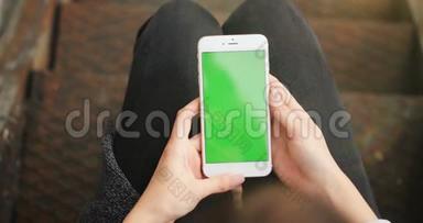 手握白色手机，大腿户外楼梯上有空白绿色屏幕