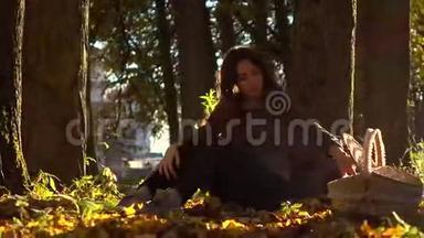 秋天的森林里，美丽的黑发女孩带着野餐篮子<strong>坐在树下</strong>。 温暖的晴天。 4Ksteatam视频