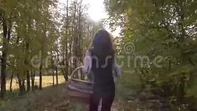 美丽的黑发女孩走过秋天的树林，拿着一个野餐篮。 晴天。 4Ksteatam视频