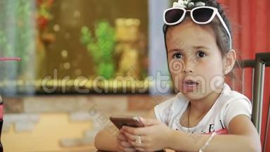 小女孩黑发拉蒂娜坐在咖啡馆里，玩智能手机游戏，愤怒，不开心