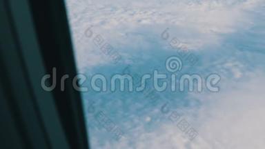 飞机的机翼穿过舷窗。 飞机飞过美丽的空中云层