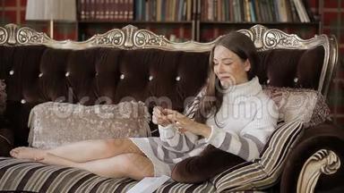 美丽的白种人女人穿着白色毛衣躺在沙发上，手里拿着明信片。