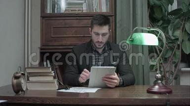 年轻人坐在办公桌前，在<strong>家</strong>里的办公室里用<strong>数码</strong>平板电脑看书