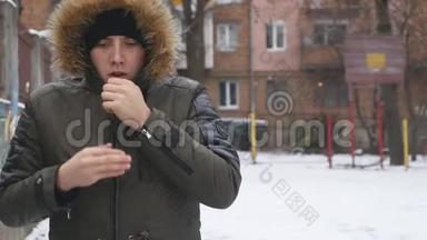 戴着黑帽子的年轻人在寒冷的冬天天气里暖手的肖像。 快关门。 户外活动