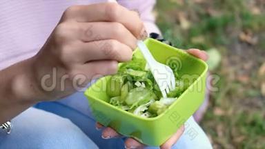 一个女人在美丽的晨光中拿着一盘新鲜的绿色沙拉。 健康饮食