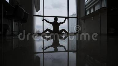 窗前一位年轻体操运动员的剪影和倒影。 一个穿麻绳的女孩正在窗边做运动。
