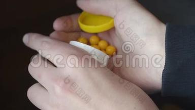 男人手里拿着一个白色<strong>聚合</strong>物药罐，里面有黄色维生素在黑暗的背景上。 一个人
