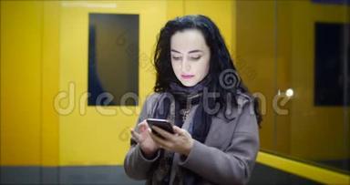 有魅力的女人在<strong>夜晚</strong>城市的节日灯光的背景下，一边使用手机，一边穿过<strong>街道</strong>。