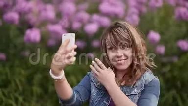 一个年轻的女孩在你的手机上拍照，在花丛中自拍。