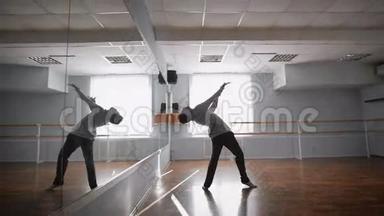 年轻漂亮的舞者在舞厅的镜子附近跳跃和旋转。 穿灰色套头衫的<strong>舞蹈团</strong>成员