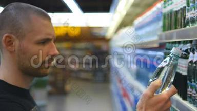 年轻人在<strong>超市</strong>里选择和购买一瓶矿泉水。 从<strong>杂货</strong>店货架上拿产品的家伙