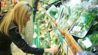 一个女人在<strong>蔬菜</strong>货架上的超市里买<strong>蔬菜</strong>和<strong>水果</strong>。 男人选择绿色