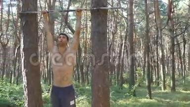 运动型肌肉男，具有完美的健身身体，在森林的水平杆上进行腹部运动。 男子