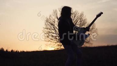 日落时分，人们在靠近树的田野里弹电吉他，唱抒情歌曲。 剪影