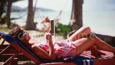 戴着太阳镜的漂亮女人在沙滩椅上用笔记本电脑工作。 1920x1080