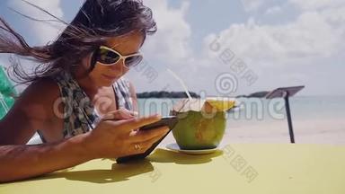 年轻的黑发美女，戴着太阳镜，在海滩上聊天，喝着<strong>椰子</strong>做的<strong>鸡尾酒</strong>