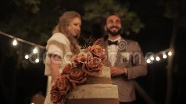 新娘和新郎靠近婚礼蛋糕。 夫妇切婚礼蛋糕Rustic。 室外