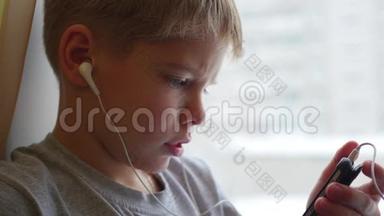 孩子坐在窗台上，用耳机特写在智能手机上听音乐