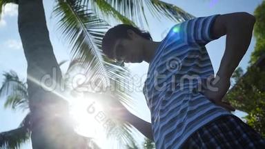 年轻人戴着太阳镜，在室外使用移动智能手机，在棕榈树下使用太阳和激光照明效果。 慢慢