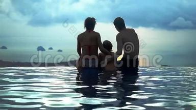 爸爸妈妈抱着儿子坐在水池边，在山顶上看到无限的海景，动作缓慢