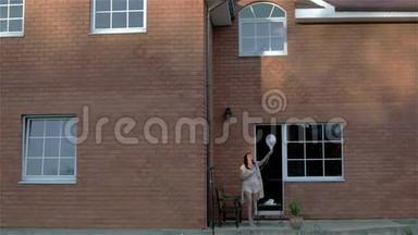 一个穿着睡衣的女人正在家里的<strong>门廊</strong>上出去，在天空中发送一个气球。