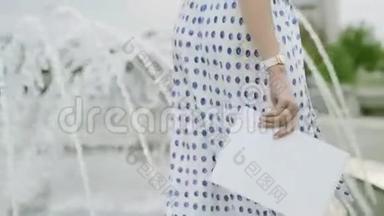 一个穿着夏装的女人，带着一张纸在喷泉周围走来走去。