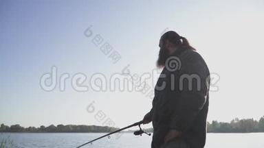有胡子的人正在河岸上钓鱼。在河里用鱼竿钓鱼的渔夫。河里钓鱼。慢
