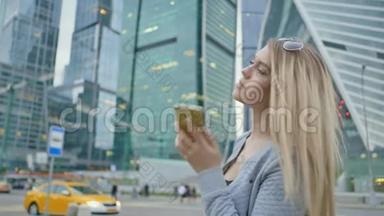 在市中心摩天大楼和高楼大厦的背景下，一个金发女孩正在打电话。