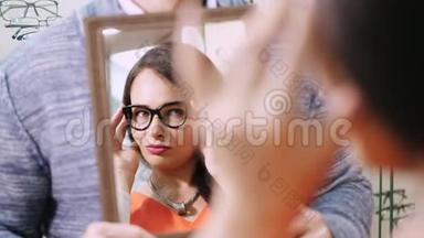 年轻女子在眼镜店用镜子检查她的新眼镜。 戴眼镜的年轻女子