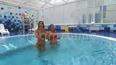 两个美丽的女人在镜头前挥手致意，互相泼<strong>水</strong>，<strong>站</strong>在游泳池里